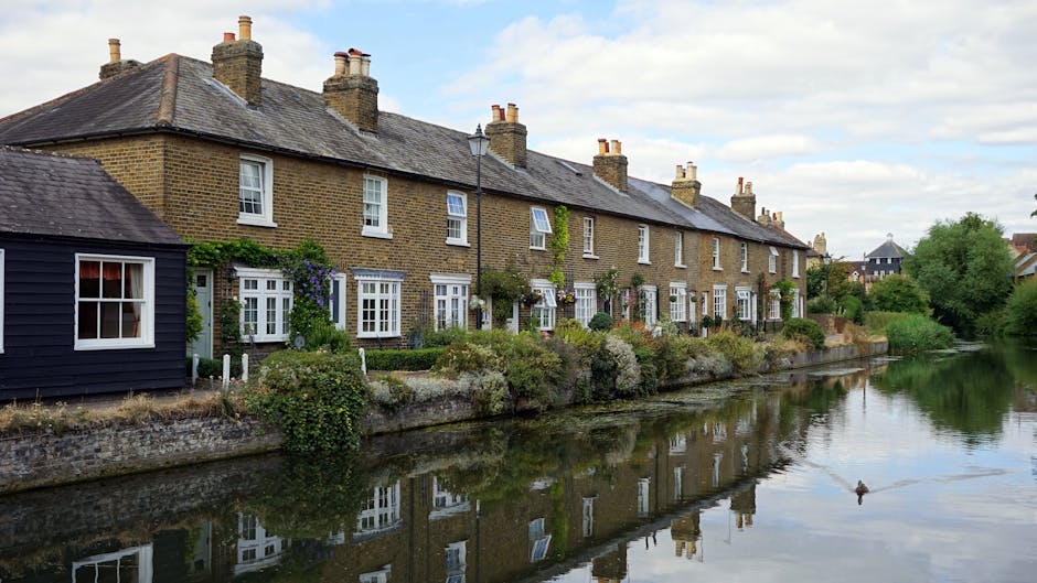 Image of a row of Victorian-style terraced residential buildings constructed with light brown and beige bricks, featuring large white-framed sash windows and black wrought iron railings along the fron
